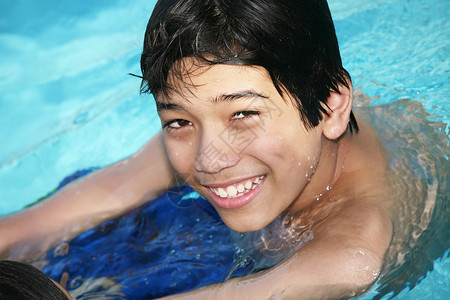 年轻男孩在游泳池游泳晴天乐趣活动男生水池混血微笑福利阳光混血儿背景图片