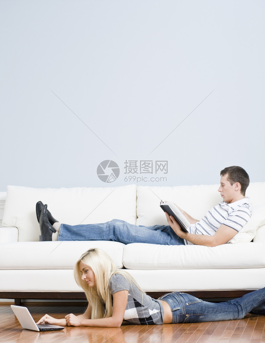 在客厅放松一对夫妇蓝色电脑伙伴牛仔裤闲暇丈夫女士长椅男人笔记本图片
