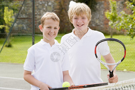 两个年轻男性朋友在网球场上笑着拍拍拍打哥们儿童年孩子网球球拍男生游戏队友青春期男孩们背景图片