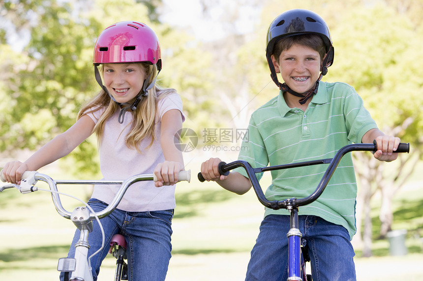哥哥和姐姐在户外的自行车上微笑着笑兄弟女孩公园相机男生女性安全帽骑术享受水平图片