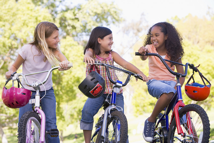 三名年轻女孩朋友在户外 骑着自行车微笑着笑朋友们公园骑术女孩们团体最好的朋友三个人头盔团伙水平图片