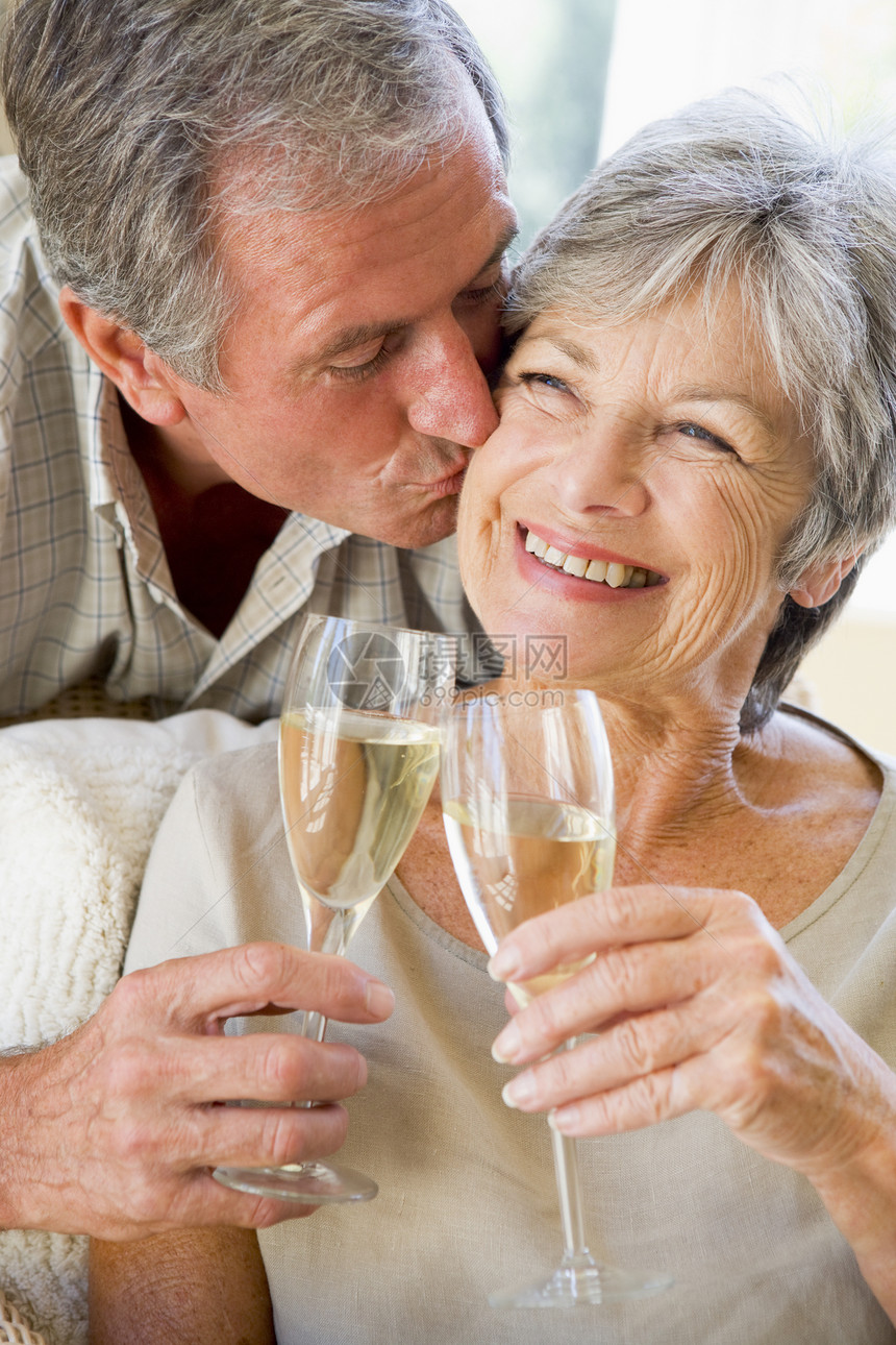 在客厅的一对夫妇为香槟干杯 亲吻和微笑图片
