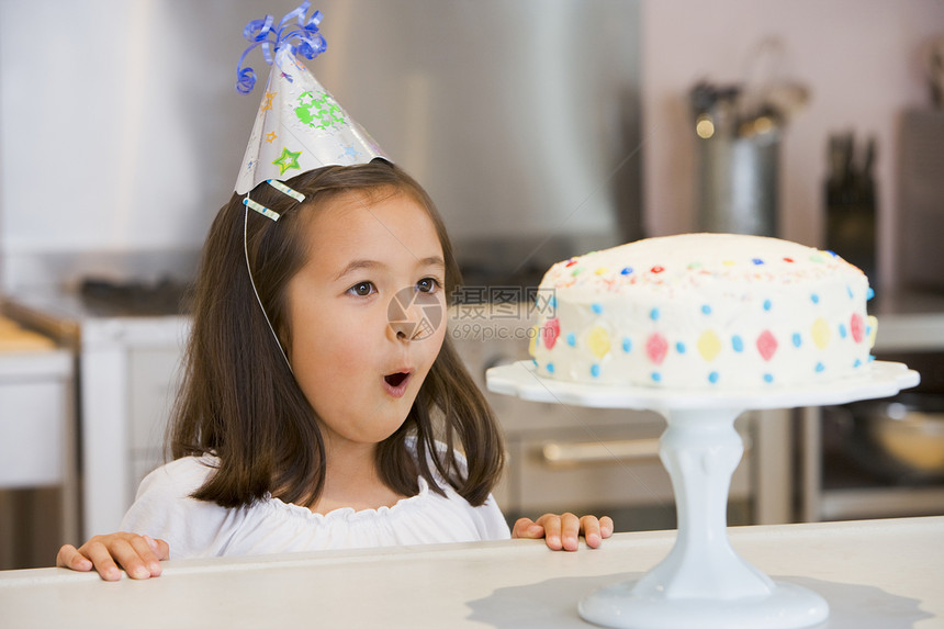 在厨房柜台戴党帽的年轻女孩 看着蛋糕图片