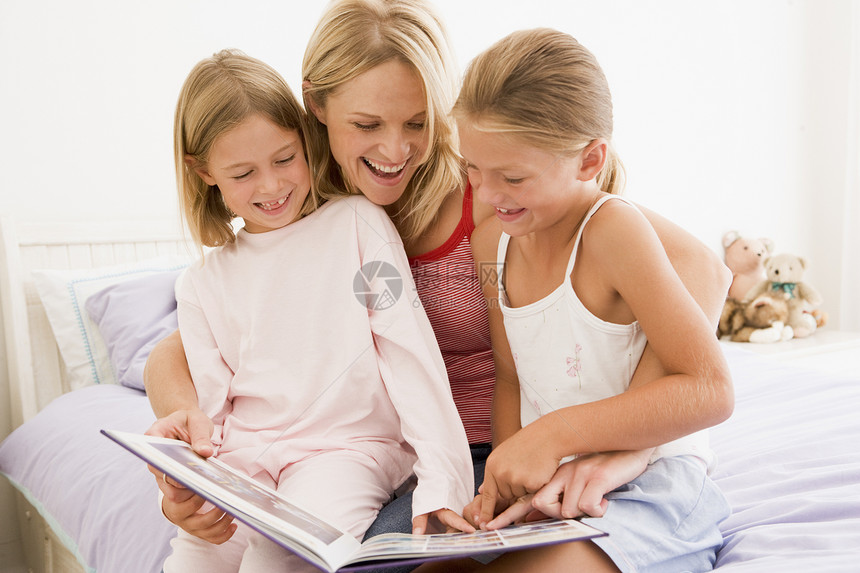 女人和两个年轻女孩 在卧室阅读书和微笑中图片