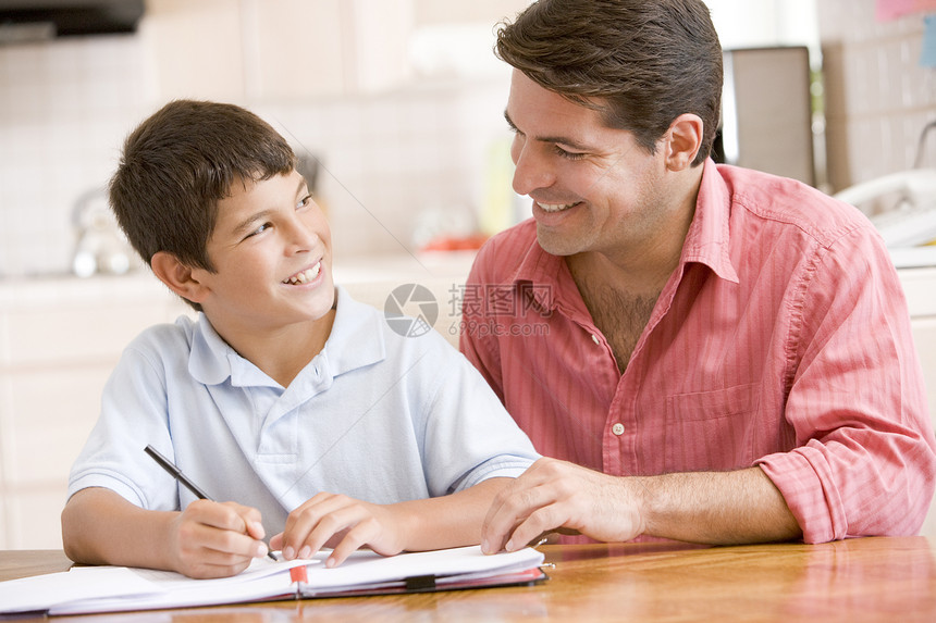 男人在厨房帮助小男孩做功课和微笑两个人孩子笔记监督桌子家庭作业爸爸儿子拉丁写作图片