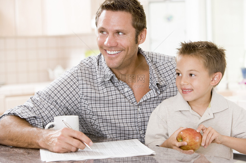 厨房里的男人和男孩 有苹果和咖啡面容的报纸图片
