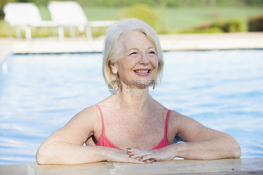 在户外游泳池中微笑着的女子游泳衣相机女性享受女士游泳退休水平图片