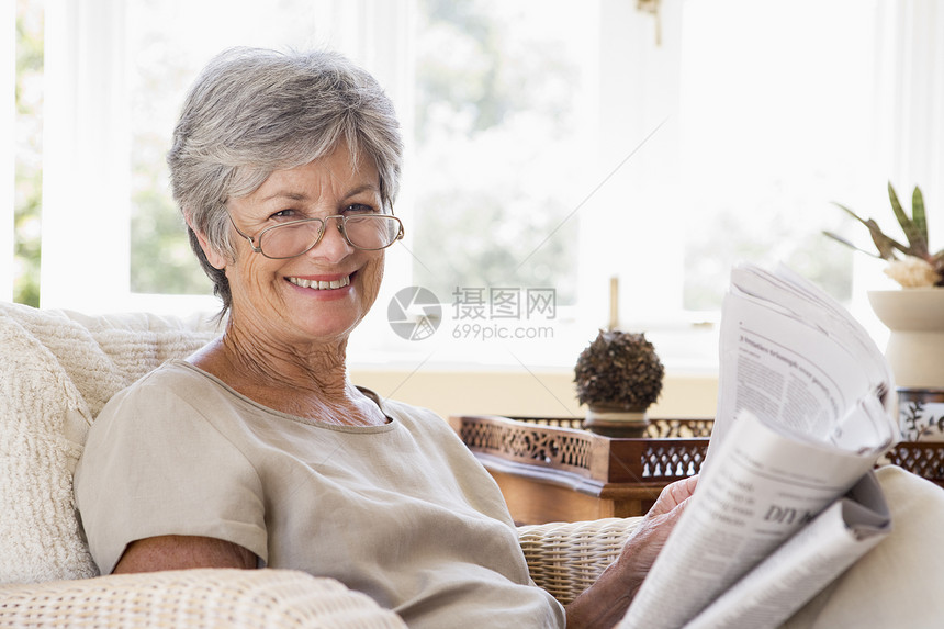 妇女在起居室阅读报纸上微笑客厅眼镜长椅女性沙发退休水平女士相机休息室图片