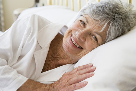 女人躺在床上笑着微笑水平女士退休苏醒睡眠休息相机卧室睡衣女性背景图片