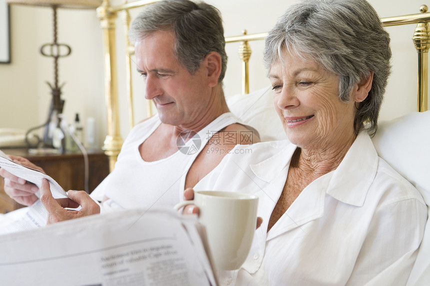 在卧室的夫妇 咖啡和报纸笑着微笑退休苏醒夫妻一杯茶丈夫两个人阅读水平女性睡衣图片