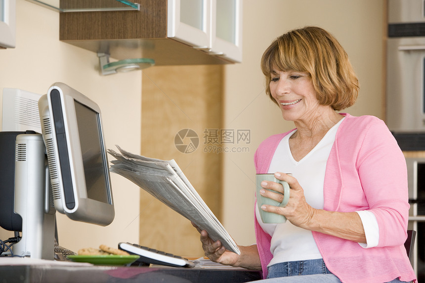 厨房里的女人 带着报纸和咖啡笑着的咖啡一杯茶工作站女性技术电脑冲浪成人互联网桌子微笑图片