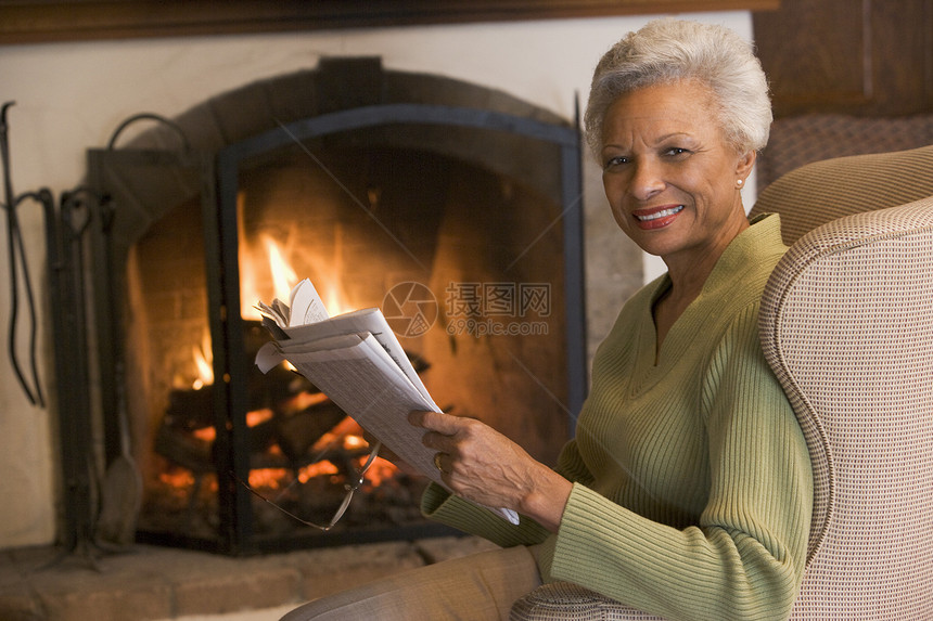 坐在壁炉边起居室的妇女 报纸微笑着图片