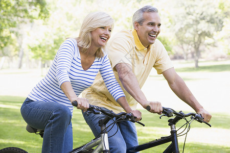 一对在户外骑自行车的夫妇微笑着男人男性婴儿潮男朋友公园享受中年女性骑术两个人背景图片