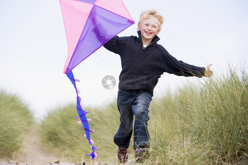 小男孩在海滩上奔跑 风筝微笑男性孩子们季节中年小路跑步途径沙丘孩子低角度图片