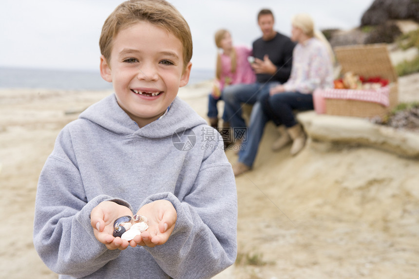 家人在海滩上野餐 微笑着以带贝壳的男孩为焦点图片