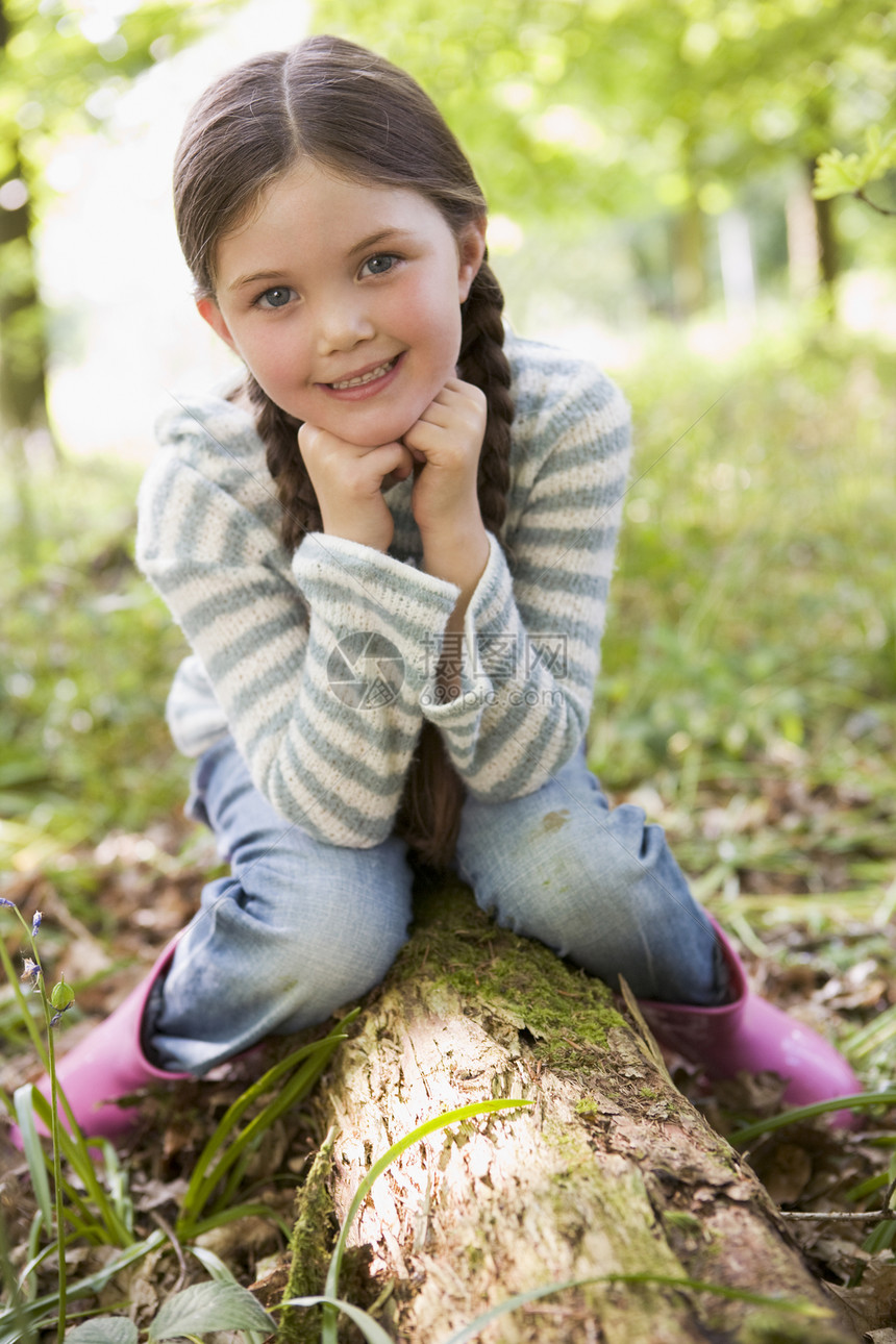 坐在树木上笑着的树林里的年轻女孩微笑森林公园相机农村雨靴靴子女性林地橡胶图片