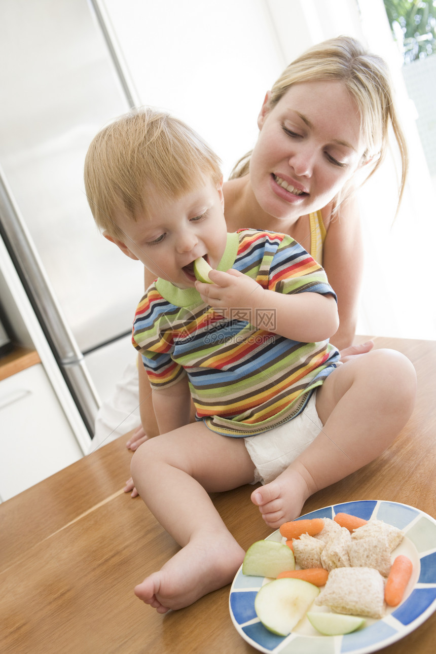 母亲和婴儿在厨房里吃水果和蔬菜图片