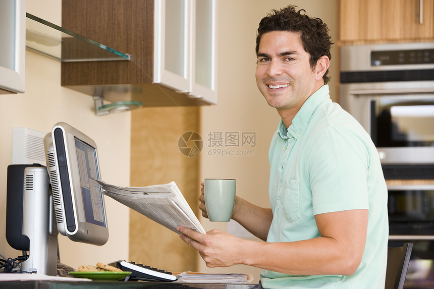 厨房里的男人 拿着电脑的报纸和咖啡面浆图片