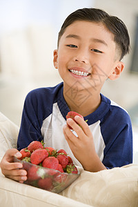 坐着草莓男孩小男孩在客厅吃草莓时微笑着笑头肩享受偏移角食物孩子们食品儿童孩子健康饮食水果背景