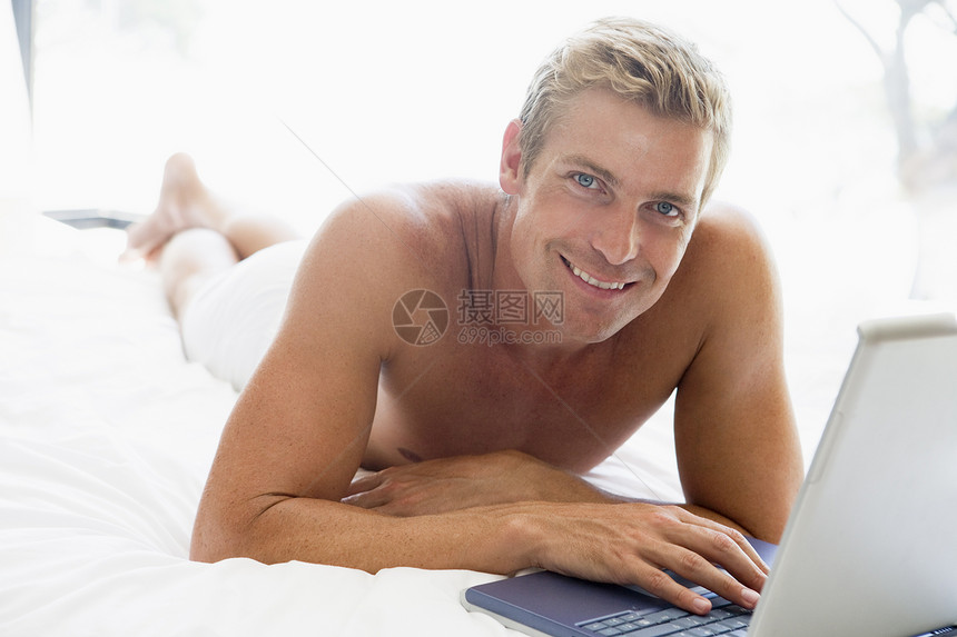 男人躺在床上 带着笔记本电脑微笑中年成人技术卧室互联网水平双人床上网世代男性图片