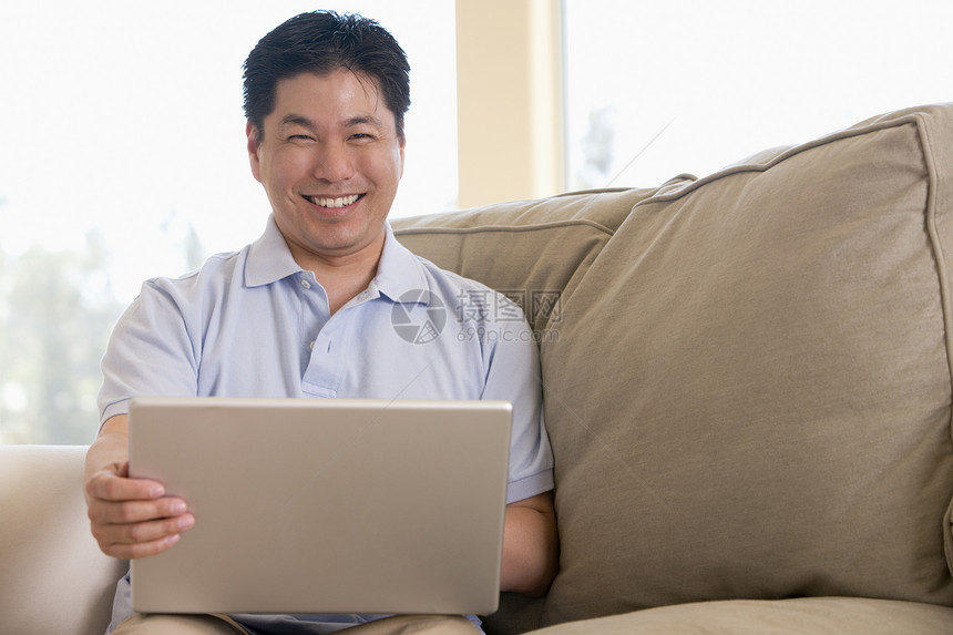 使用笔记本电脑和微笑在客厅里的人成人男性沙发互联网家庭上网水平中年长度相机图片