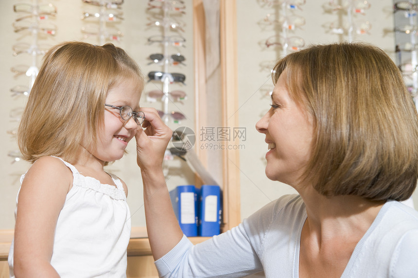 妇女用眼镜对着在观光家微笑的年轻女孩试戴眼睛眼镜水平女性中年夫妻商业妈妈卫生框架帮助母亲图片