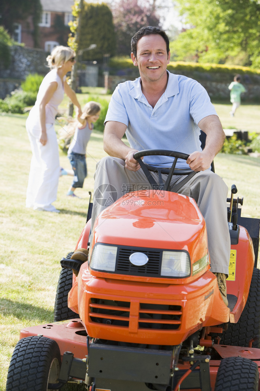 户外男子驾驶草坪除草机 与背景家庭一起微笑图片