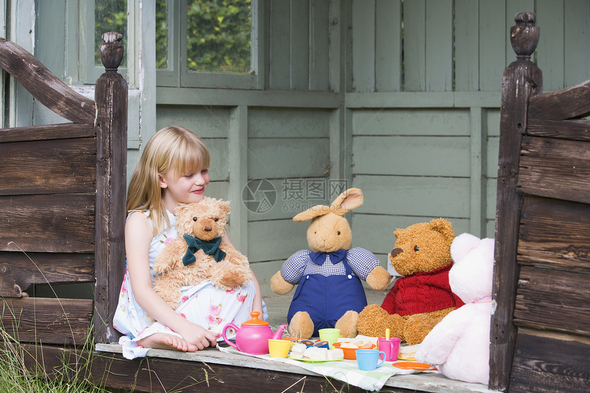 年轻女孩在小屋玩茶和微笑娃娃水平一杯茶凉亭毛绒动物花园乐趣想像力后院图片