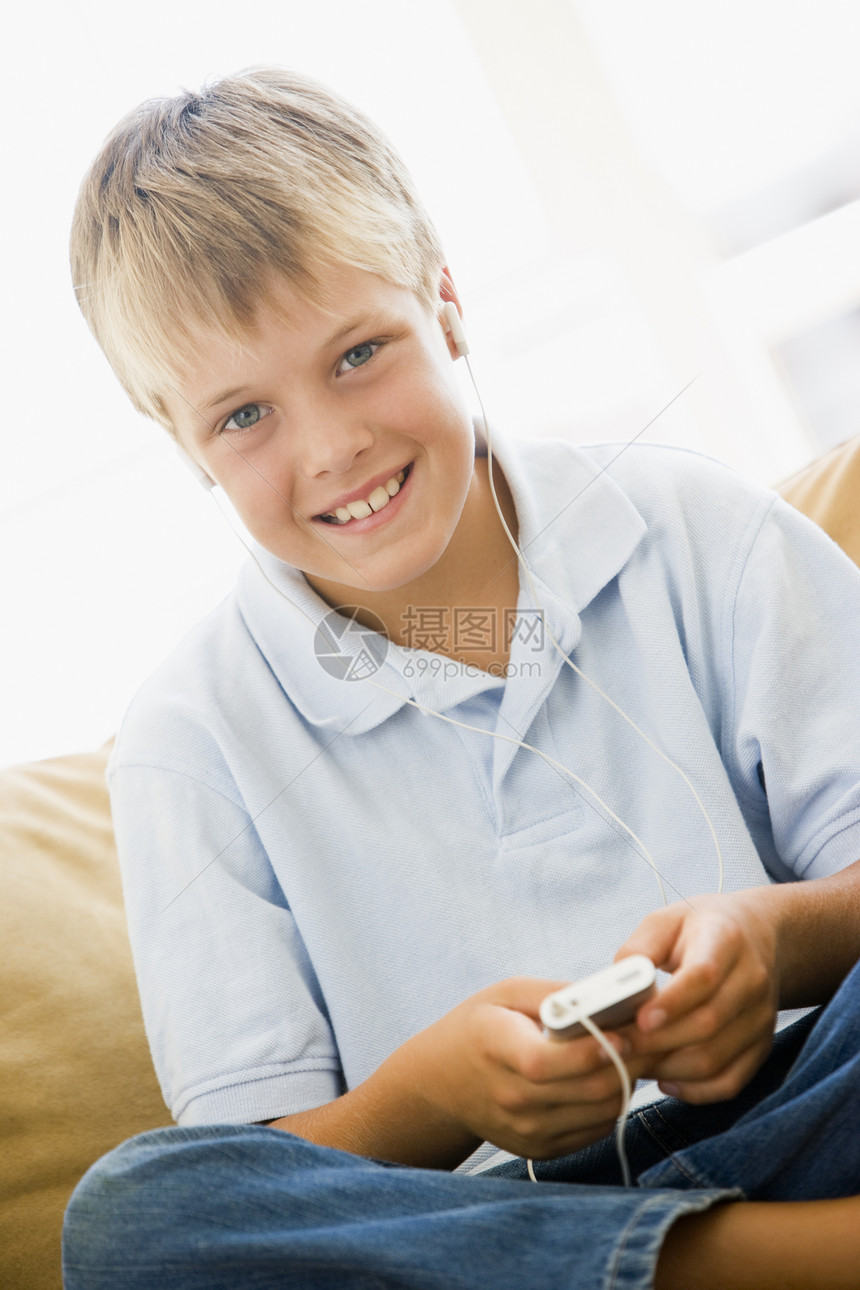 在客厅的年轻男孩 与MP3玩家微笑孩子们孩子技术座位音频音响长椅享受设备音乐图片