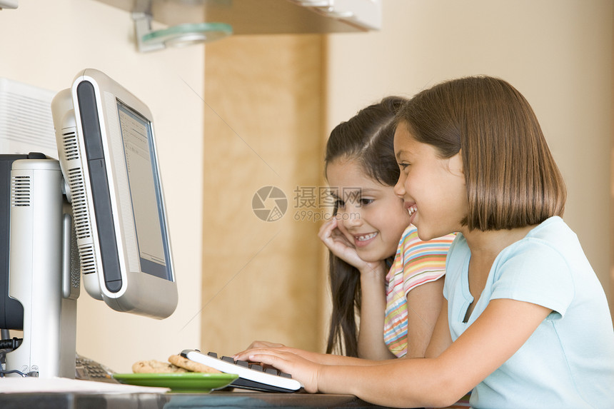 两个年轻女孩在厨房 带着计算机微笑的电脑图片