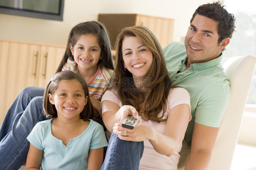 家庭在起居室 遥控器微笑沙发拉丁爸爸享受母亲电视四个人妈妈频道休息室图片