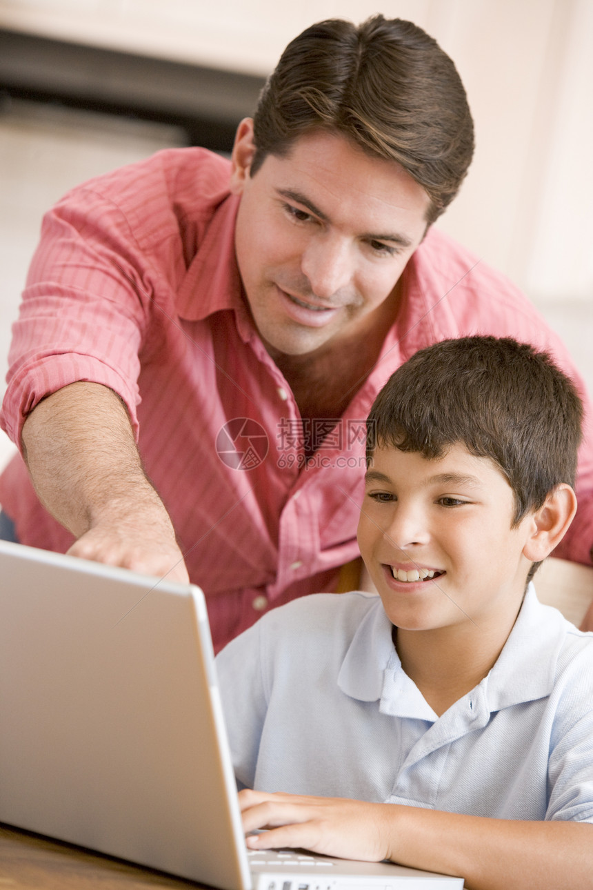 男人笑着用笔记本电脑在厨房帮助小男孩男生互联网桌子家长儿子冲浪男性爸爸孩子们拉丁图片