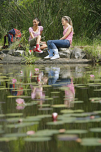 荷叶池塘的女孩坐在溪边的青年妇女背景