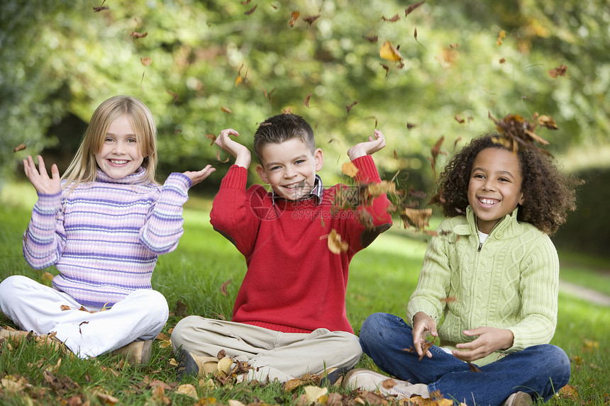 三名儿童坐在户外公园中微笑着笑容的小孩爸爸父亲们成年人孩子们孩子落叶叶子家庭外表情感图片