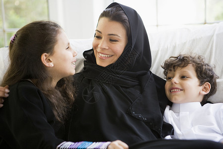坐在客厅里的母亲和两名幼儿笑着高关键选择性重点焦距成年人阶段家庭孩子外表窗户图书女孩感情背景图片