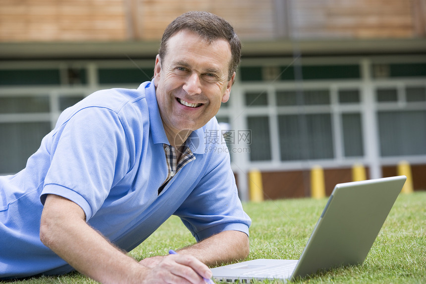 男人用笔记本电脑躺在学校草坪上休闲服眼神婴儿教育学生大学服饰成人教育情绪相机图片
