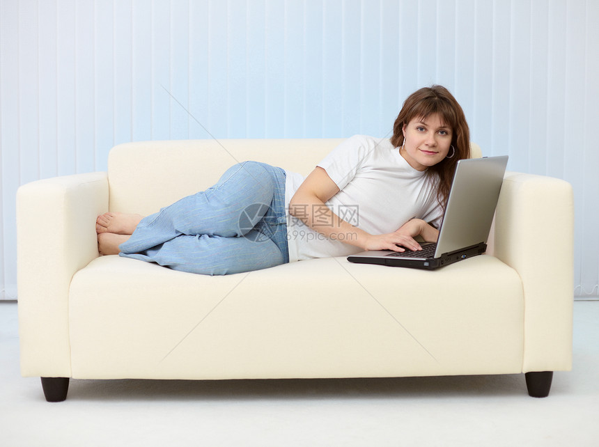 沙发上有笔记本电脑的年轻美女赤足蓝色女性褐色女士女孩长沙发家具键盘白色图片