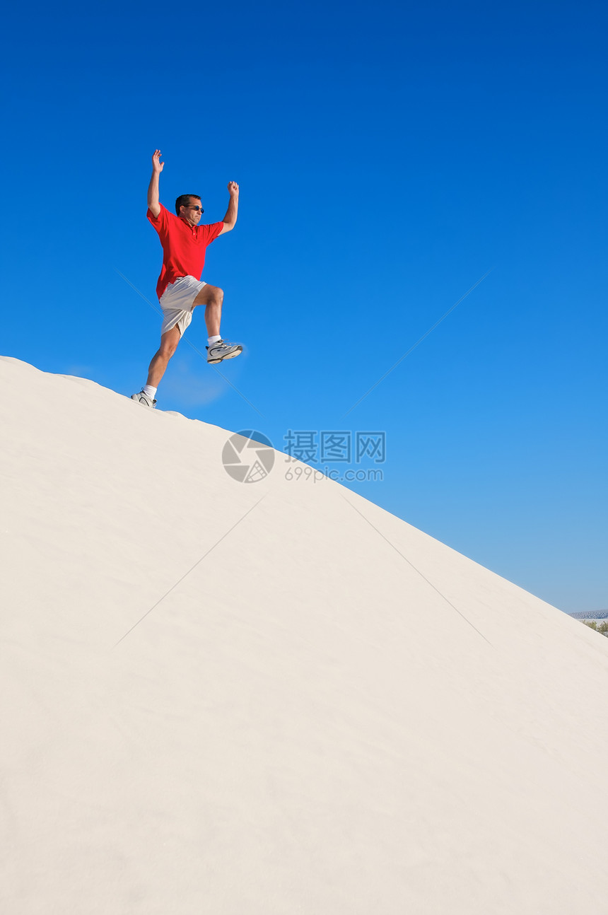 穿红衬衫的人 从白沙丘顶上跳跃图片