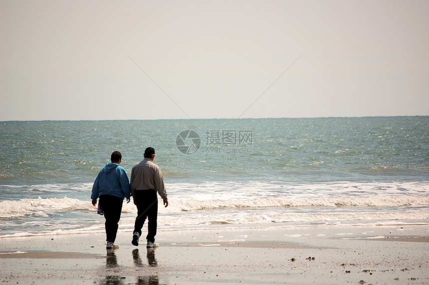 老年夫妇在海滩上散步海洋冲浪波浪图片