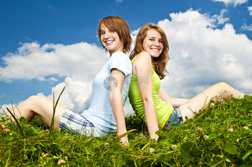 坐在草原上的年轻女孩女朋友绿色乐趣花朵友谊女性喜悦闺蜜场地享受图片