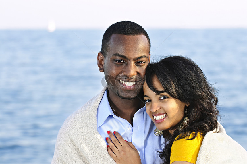 快乐的夫妻共享毯子海滩男人女士少数民族闲暇海洋幸福微笑假期温暖图片