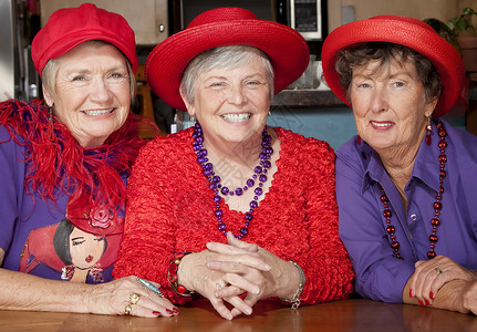 三名身戴红色帽子的高级妇女紫色三重奏女性蟒蛇快乐项链老年团体乐趣朋友背景图片