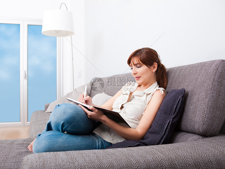 在家学习的妇女享受长椅快乐女性女孩笔记沙发女士笔记本牛仔裤图片