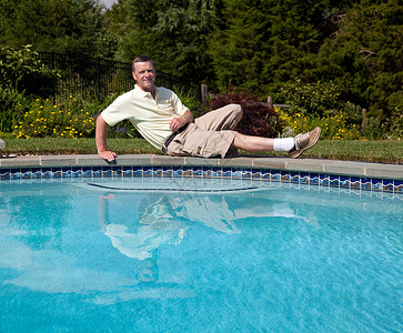 横卧按游泳池分列的老年男性背景