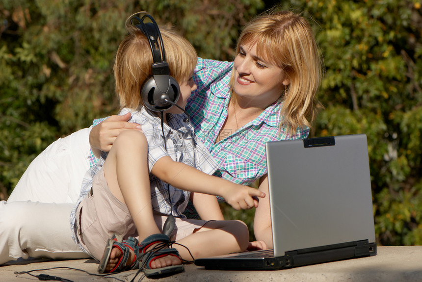 在公园里拿着笔记本电脑的小男孩和母亲成人自由耳机女性沉思妈妈午休衣服享受工作图片