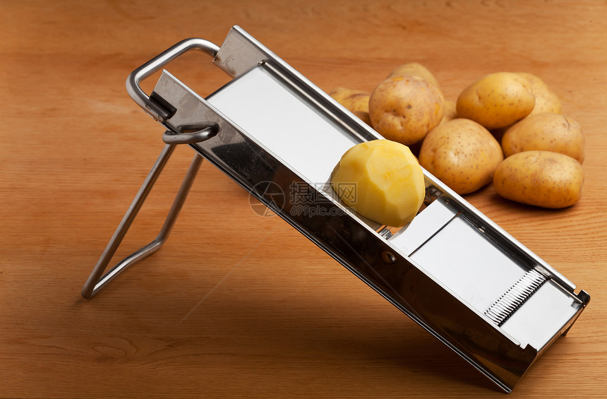 曼陀林切片机上半个马铃薯用具厨房反射桌子食物蔬菜木头橡木刀刃金属图片