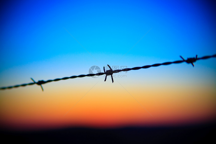 特写在日落天空滴下刺铁丝网橙子监狱危险铁丝网边缘金属日出地标太阳栅栏图片