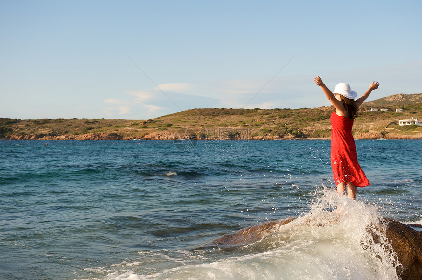 美丽的女孩在海浪中飘荡石头岩石热带太阳乐趣假期气候帽子女性自由图片