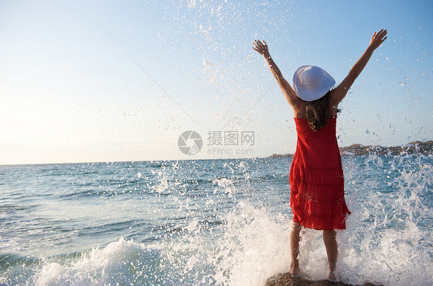美丽的女孩在海浪中飘荡日落海滩气候帽子岩石女性乐趣太阳幸福假期图片