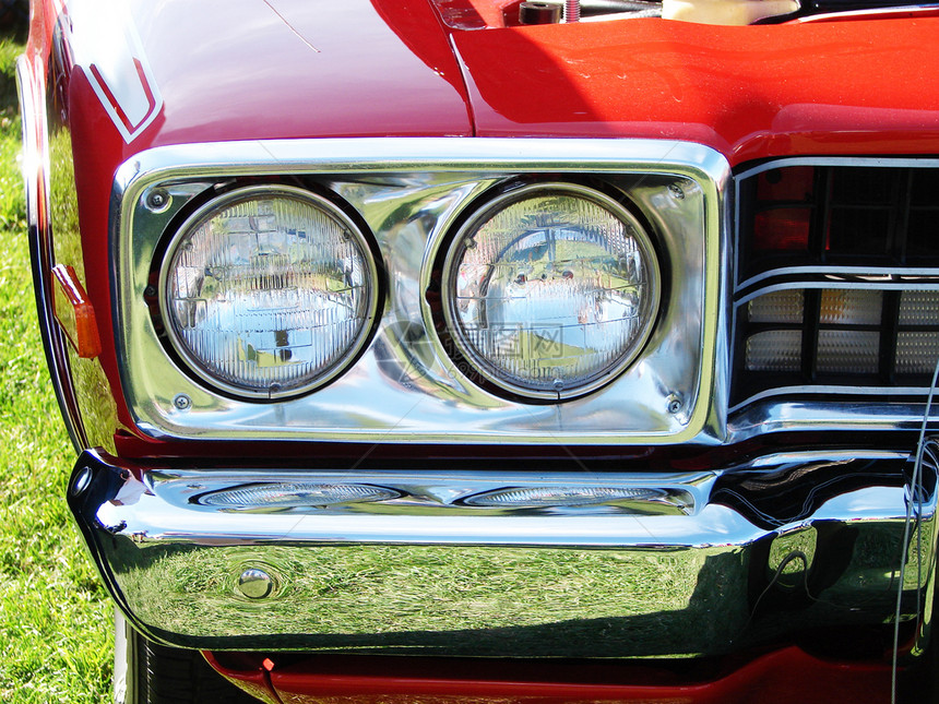 一辆明亮红色肌肉车的头灯和铬保险杠图片